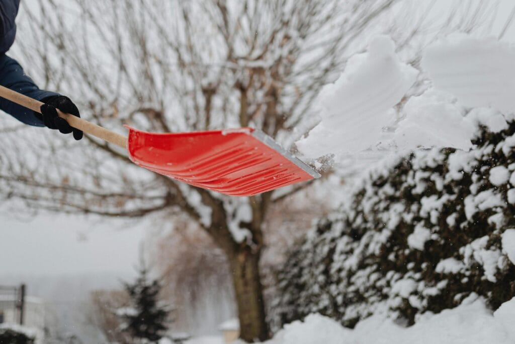 pexels-photo-6952501-6952501 Person using a bright red shovel to clear snow in a winter landscape.